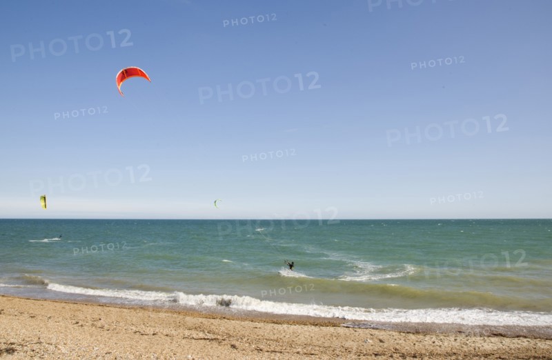 ENGLAND, West Sussex, Lancing, Kite Surfers on sea next to shingle beach in the summer with blue sky