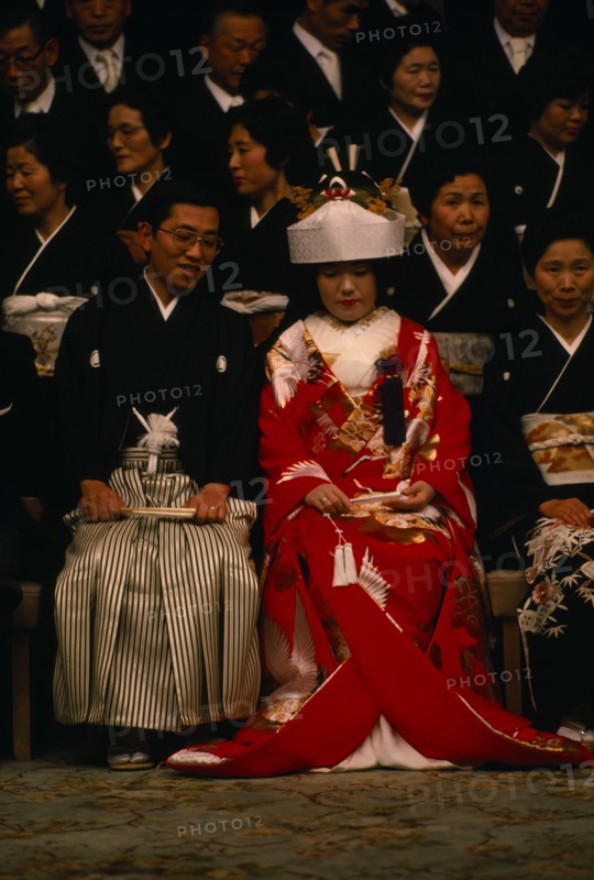 JAPAN, Honshu, Tokyo, Seated bride and groom and guests attending Shinto wedding ceremony wearing traditional dress before changing into western style clothes for later party.