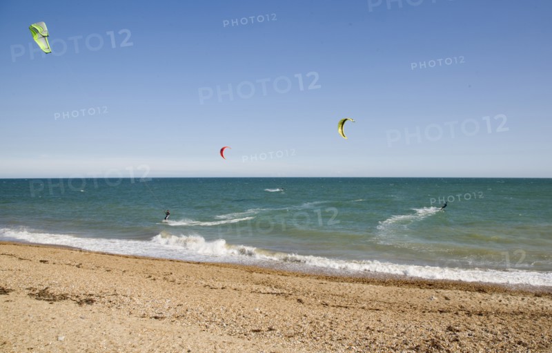 ENGLAND, West Sussex, Lancing, Kite Surfers on sea next to shingle beach in the summer with blue sky