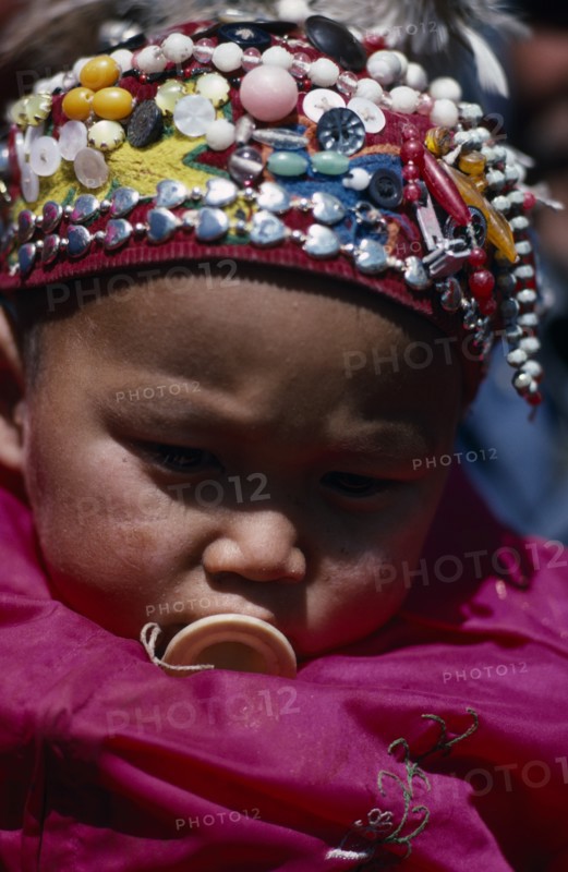 CHINA, Xinjiang Province, Altai Region, Portrait of Kazakh baby wearing hat covered with silver beads and coloured buttons.