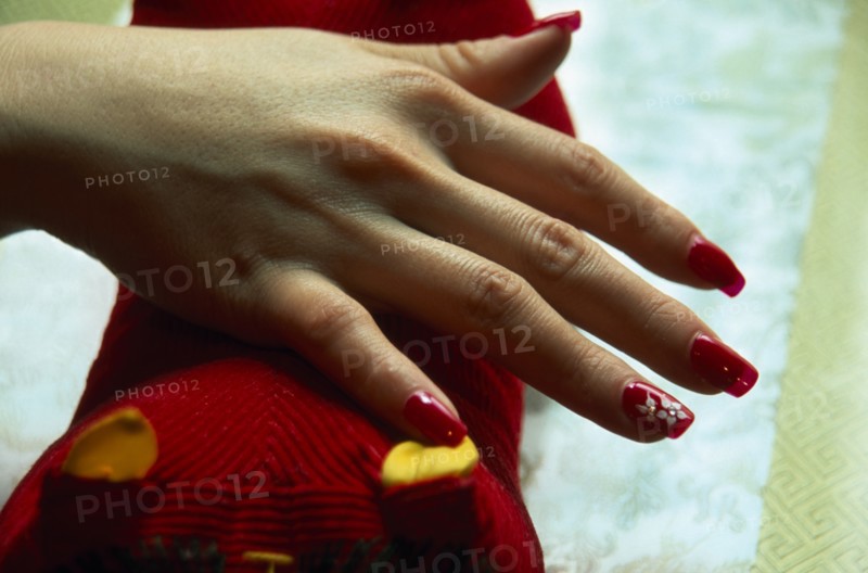 CHINA, Beijing, "Close cropped shot of manicured and painted nails with red nail polish, white flower detail and jewel type additions."