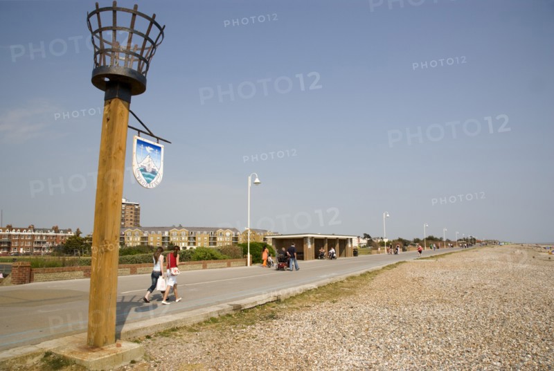 ENGLAND, West Sussex, Littlehampton, People walking along the promenade next to shingle beach with a torch beacon in the foreground