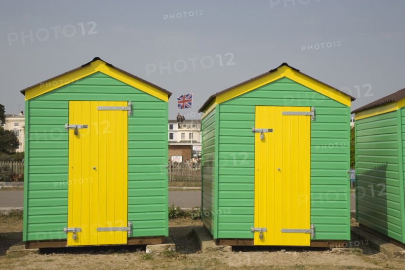 ENGLAND, West Sussex, Littlehampton, Green and yellow beach huts next to promenade with a Union Jack flag seen behind