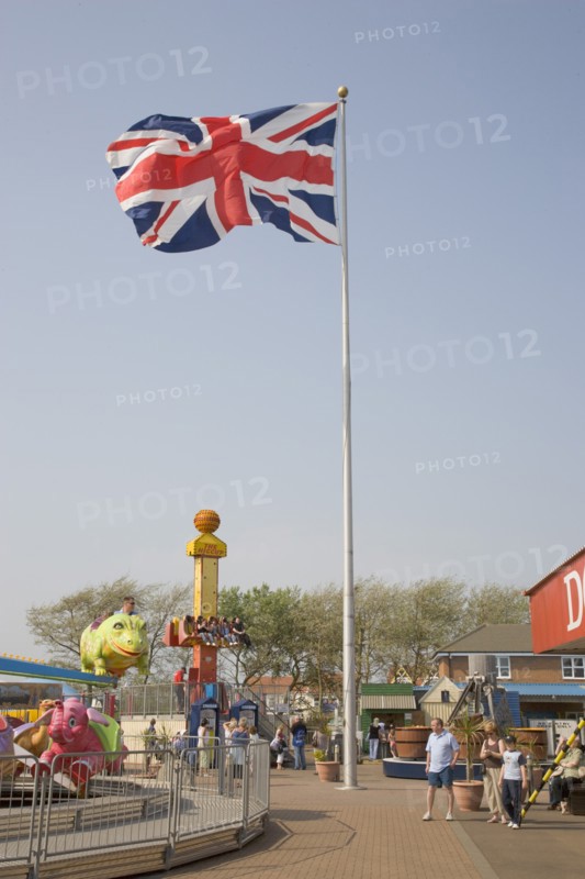 ENGLAND, West Sussex, Littlehampton, Harbour Park Amusements with families enjoying rides.  British Union Jack flag flying in the wind against a blue sky