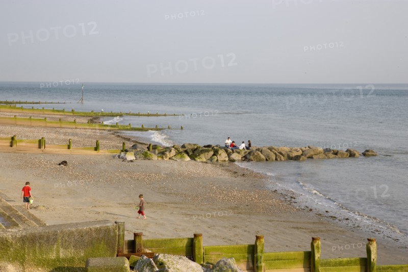 ENGLAND, West Sussex, Selsey, Children playing with bucket and spade on sandy beach next to sea