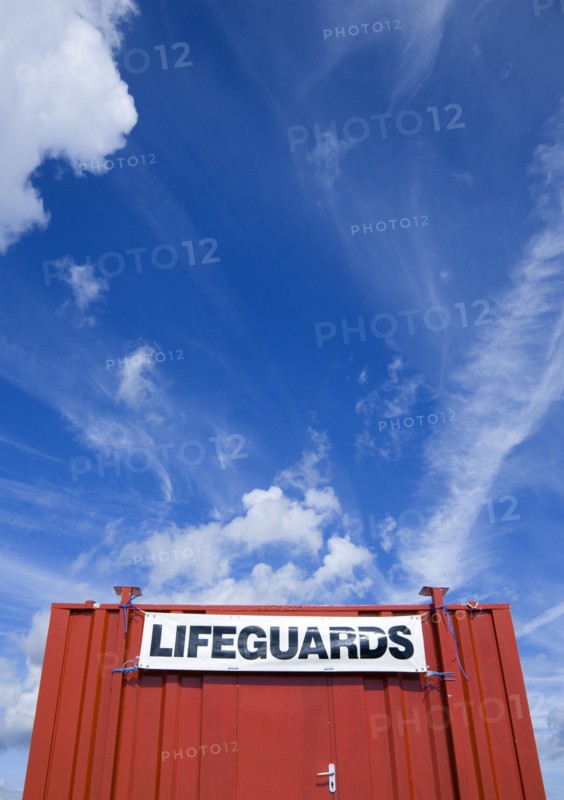 ENGLAND, West Sussex, Littlehampton, Red shipping container used as a lifeguards hut on the beach with expansive blue sky overhead