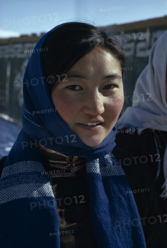 MONGOLIA, People, Altai provincial capital in winter. Head and shoulders portrait of young woman wearing fleece lined traditional tunic and modern woollen blue headscarf. East Asia Asian Female Women Girl Lady Mongol Uls Mongolian