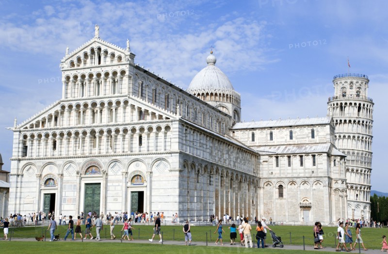 ITALY, Tuscany, Pisa, The Campo dei Miracoli Field of Miracles. Tourists walking past the 12th Century lombard-style facade of the Cathedral or Duomo with the 14th Century Leaning Tower beyond all within the UNESCO World Heritage site