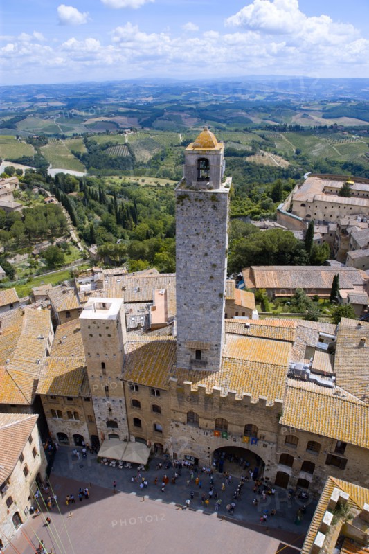 ITALY, Tuscany, San Gimignano, People in the Piazza del Duomo with the town's oldest tower of the Palazzo Vecchio Podesta built in 1239 with the farmland east of the town beyond