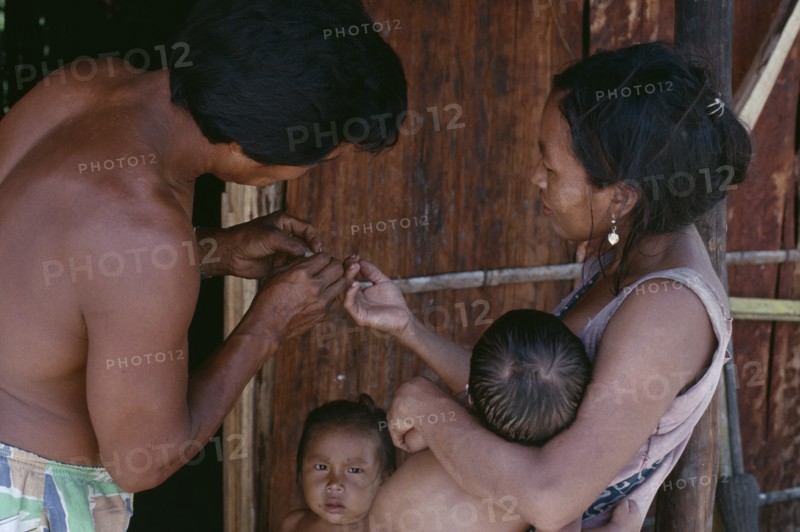 COLOMBIA, North West Amazon, Tukano Indigenous People, Makuna family.  Venancio removing thorn from his wife's finger with two young children partly seen. Tukano  Makuna Indian North Western Amazonia American Colombian Columbia Hispanic Indegent Kids Latin America Latino South America Tukano