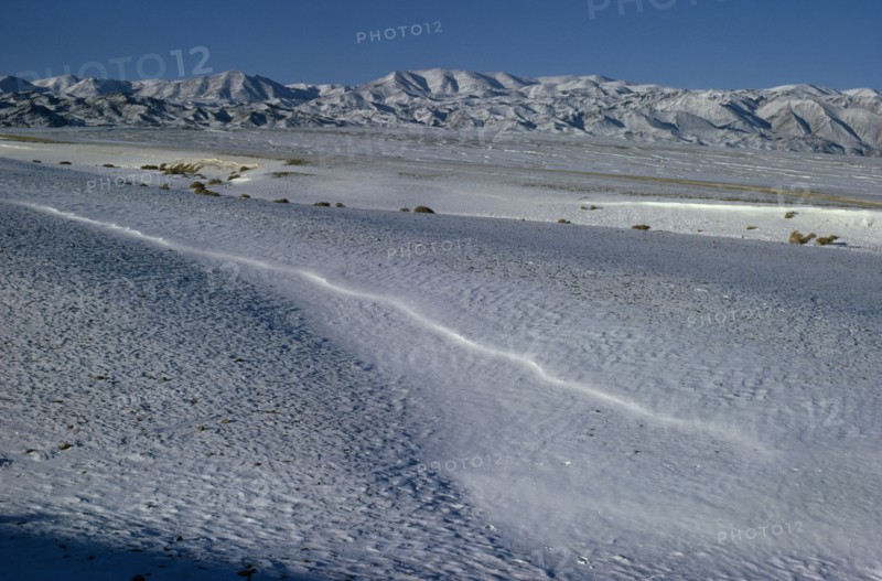 MONGOLIA, Gobi Desert, Biger Negdel, Mid-winter with snow-covered desert pastures. Onvoy of trucks brings fodder to outlying negdel collective. Altai mountains in background. East Asia Asian Mongol Uls Mongolian Scenic