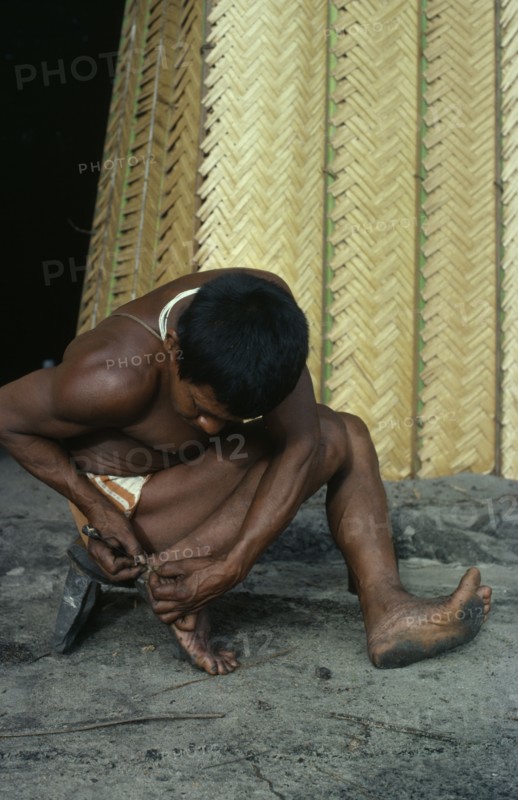 COLOMBIA, North West Amazon, Tukano Indigenous People, Barasana man removing palm spine from foot outside entrance to maloca/communal home. Tukano sedentary Indian tribe North Western Amazonia American Colombian Columbia Hispanic Indegent Latin America Latino Male Men Guy South America Tukano Male Man Guy One individual Solo Lone Solitary