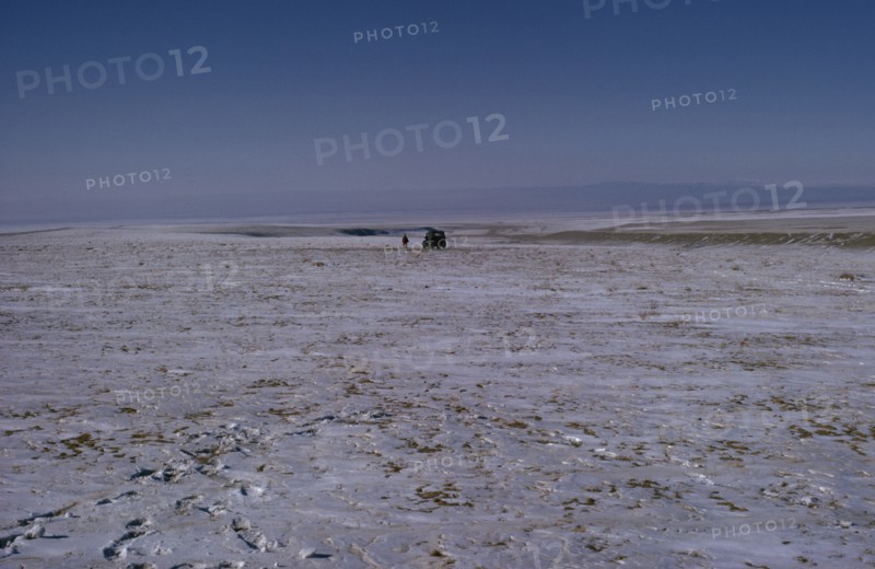 MONGOLIA, Gobi Desert, Mid-winter on the edge of the Gobi with a distant Russian Gaz jeep and lone figure walking in barren frozen landscape