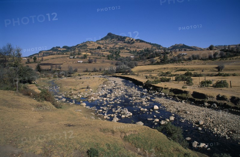 MEXICO, Michoacan State, El Rosario Butterfly Santuary, View across farmland and stream toward the butterfly sanctuary.