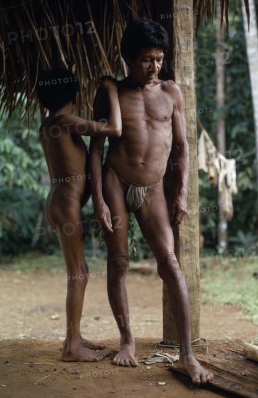 COLOMBIA, North West Amazon, Vaupes, Middle aged Maku nomad standing with his son beside frame of thatched home at base village.  indigenous tribe indian nomadic American Colombian Columbia Hispanic Indegent Kids Latin America Latino Male Men Guy South America Vaupes Male Man Guy Vaupes