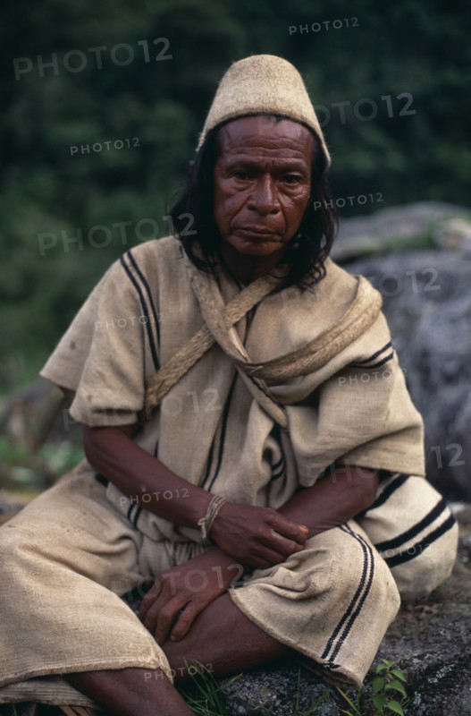 COLOMBIA, Sierra Nevada de Santa Marta, Ika, Portrait of Ika mama priest Juan de Jose wearing traditional cactus woven cactus fibre helmet and woven wool&cotton manta cloak and trousers. Fine spun cotton amulets on wrist to protect and ward off evil. Arhuaco Aruaco indigenous tribe American Colombian Colombia Hispanic Indegent Latin America Latino Religion South America  Arhuaco Aruaco indigenous tribe American Colombian Columbia Hispanic Indegent Latin America Latino Religion South America One individual Solo Lone Solitary Religious 1 Classic Classical Fiber Historical Older Single unitary
