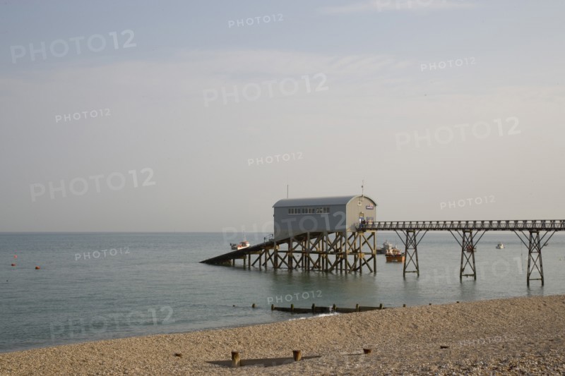 ENGLAND, West Sussex, Selsey, Royal National Lifeboat Institution. View across shingle beach towards a pier with RNLI station