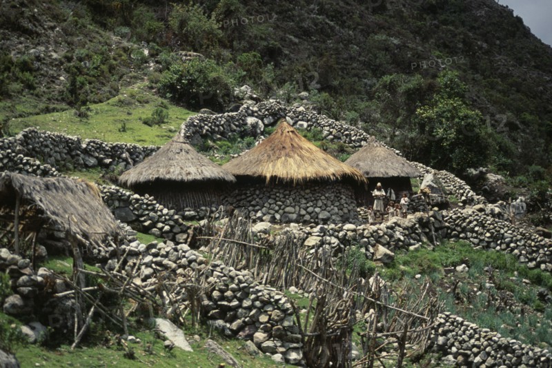 COLOMBIA, Sierra Nevada de Santa Marta, Ika Indigenous People, Ika family settlement in high Sierra  with three circular conical thatched huts and stone wall terraces set into hillside. Ika father and children standing outside central hut. Arhuaco Aruaco indigenous tribe American Colombian Colombia Hispanic Kids Latin America Latino Male Men Guy Scenic South America  Arhuaco Aruaco indigenous tribe American Colombian Columbia Hispanic Kids Latin America Latino Male Men Guy Scenic South America 3 Indegent Male Man Guy Dad