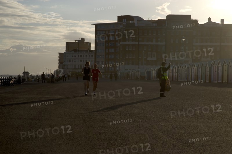 ENGLAND, East Sussex, Brighton, Silhoetted joggers on the seafront at Hove Lawns.