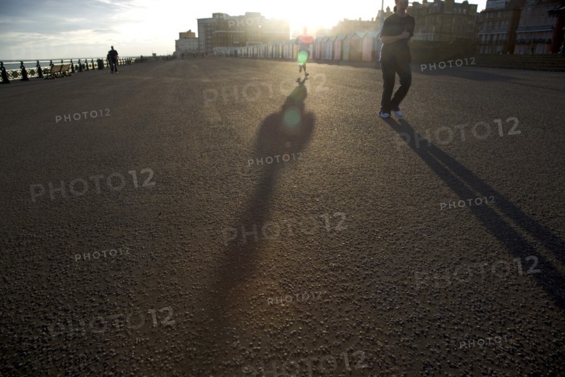 ENGLAND, East Sussex, Brighton, Silhoetted joggers on the seafront at Hove Lawns.