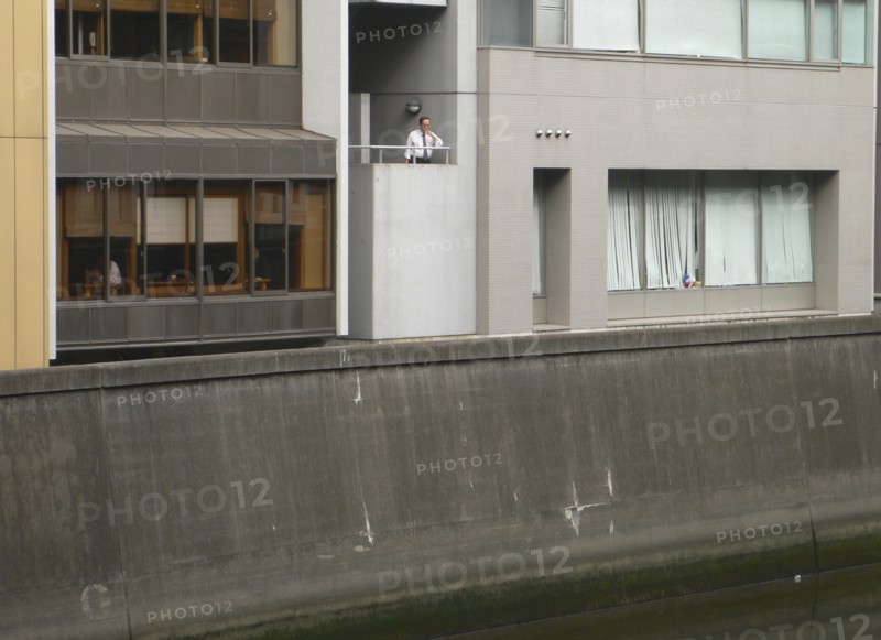 JAPAN, Honshu, Tokyo, "Nihonbashi - at lunchtime, a ""salariman"" office worker in white shirt and time takes break, smoking cigarette, looking in to Nihonbashi river, bleak urban landscape"