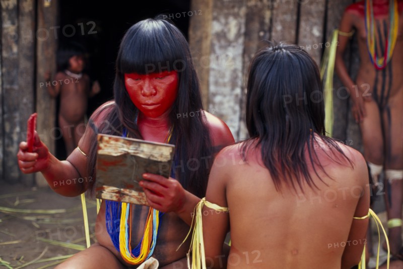 BRAZIL, Mato Grosso, Indigenous Park of the Xingu, Young Panara women applying red karajuru face and body paint in preparation for dance.   Formally known as Kreen-Akrore  Krenhakarore  Krenakore  Krenakarore  Amazon American Brasil Brazilian Female Woman Girl Lady Indegent Kreen Akore Latin America Latino South America Female Women Girl Lady Immature