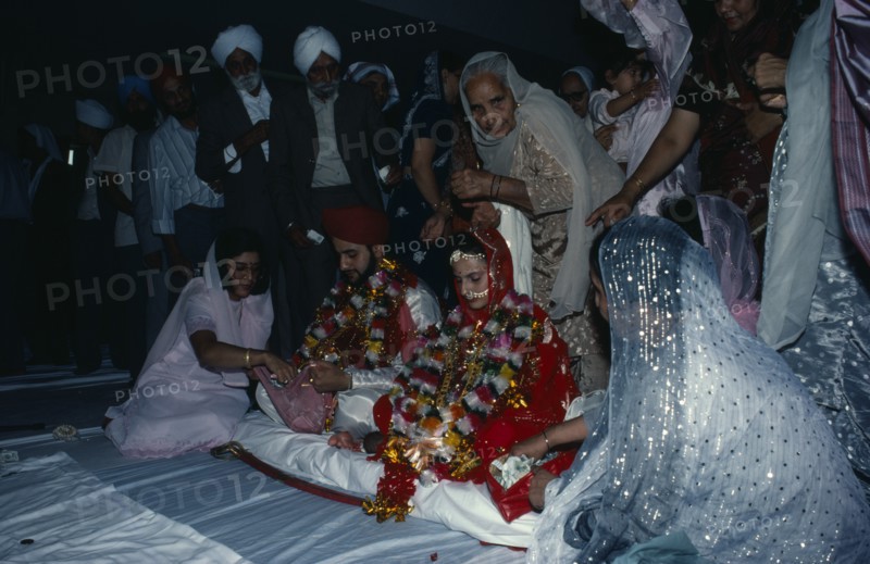 ENGLAND, Religion, Sikhism, Bride and groom receiving gifts of money from guests during wedding ceremony.