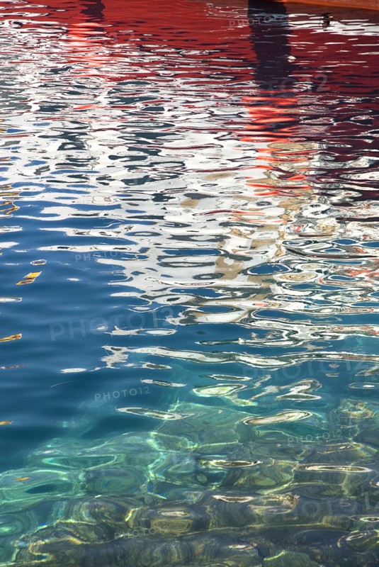 SPAIN, Canary  Islands, Lanzarote, Red and white reflection of boat in rippled water of harbour Puerto del Carmen.