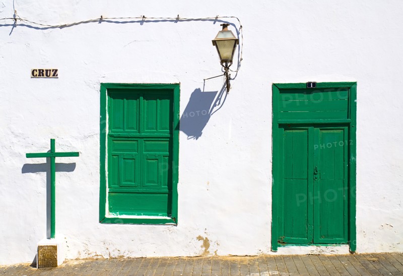 SPAIN, Canary  Islands, Lanzarote, "Teguise, former capital of the island.  Detail of house facade with typical white painted walls and green door and window shutters, cross and lantern cast shadows."