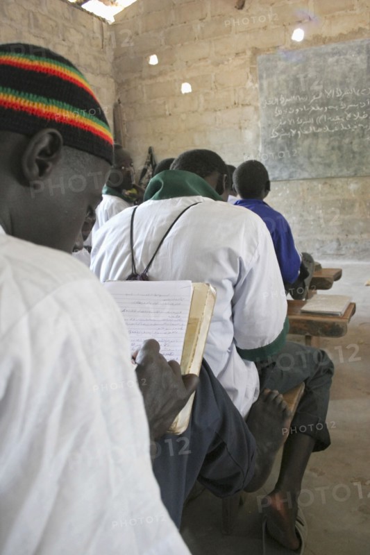 GAMBIA, Western Gambia, Tanji, Tanji Village.  Muslim boys writing in arabic at their desks while attending an islamic religious class at the Ousman Bun Afan Islamic school.  Blackboard on wall in front of them.
