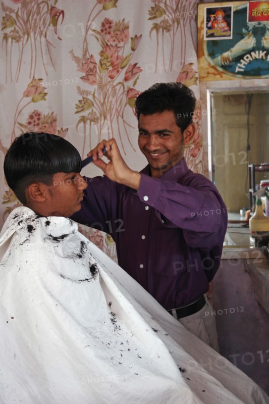 INDIA, Rajasthan, Jodhpur, Young Indian barber in his barbershop cutting the hair of a boy.