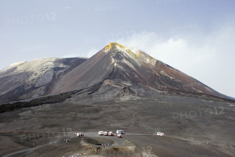 ITALY, Sicily, Mount Etna, View of active and smoking main crater of volcano and older crater with visitors and transportation vehicles in foreground.