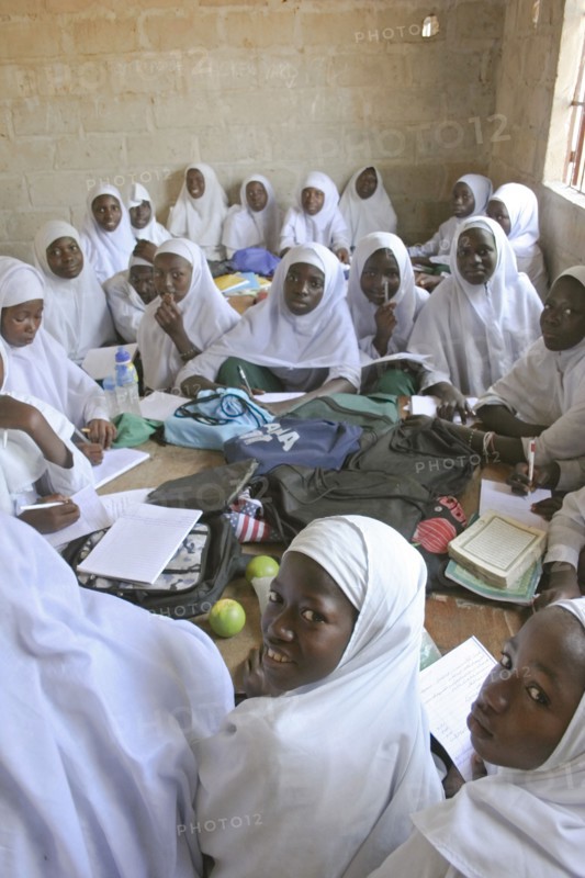 GAMBIA, Western Gambia, Tanji, Tanji Village.  African Muslim girls wearing white headscarves while attending a class at the Ousman Bun Afan Islamic school sitting in groups around desks with bags and books piled in centre.