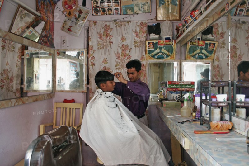INDIA, Rajasthan, Jodhpur, Young Indian barber in his barbershop cutting a boys hair.