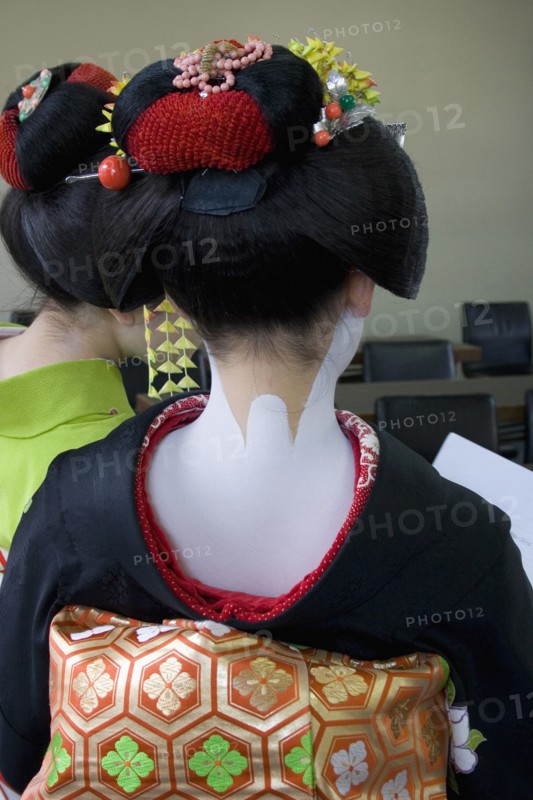 JAPAN, Honshu, Kyoto, Gion District.  Back of Geisha attending a class at Mia Garatso school for Geisha wearing black silk kimono with gold and green obi.  Hair is worn up and fixed with decorative pins and flowers exposing the unpainted nape of the neck which is considered sensuous.  Face and shoulders are painted white.