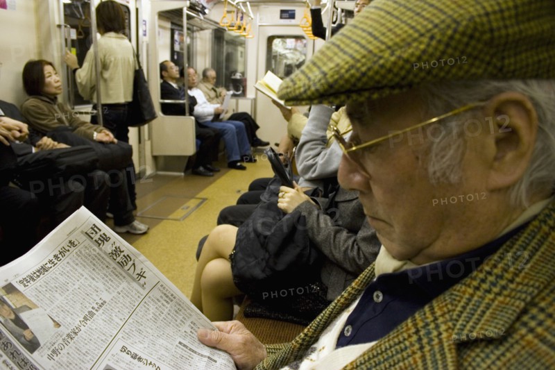 JAPAN, Honshu, Tokyo, Tokyo Metro.  Elderly Japanese man wearing tweed cap and jacket reading a newspaper while travelling on the Tokyo Metro.