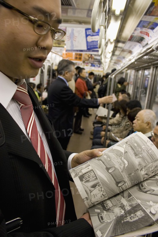 JAPAN, Honshu, Tokyo, Young Japanese man wearing a suit showing the Manga comic he is reading to the photographer while travelling on the Tokyo Metro.