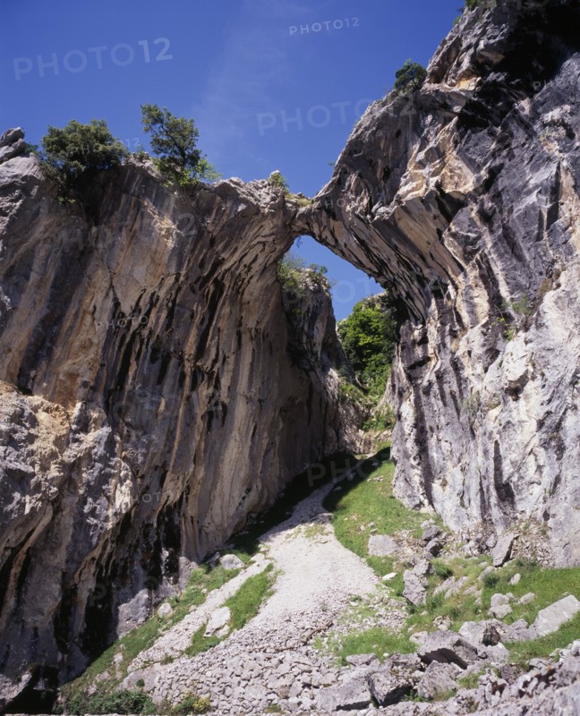 SPAIN, Asturias, Picos de Europa, Garganta del Cares.  Water eroded roofless cave in limestone cliffs framing mountain pathway and view along gorge.