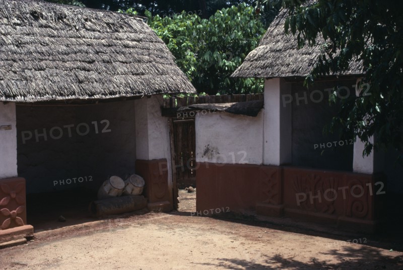 GHANA, Ashanti, Traditional thatched house with intricate patterns on walls. Ceremonial drums inside one of the huts.