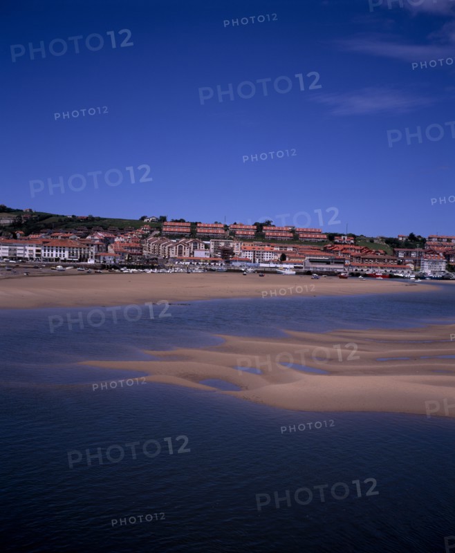 SPAIN, Cantabria, San Vicente de la Barquera, Town buildings extending to sea wall with moored boats on sand bars at low tide on the Rio del Escudo estuary.