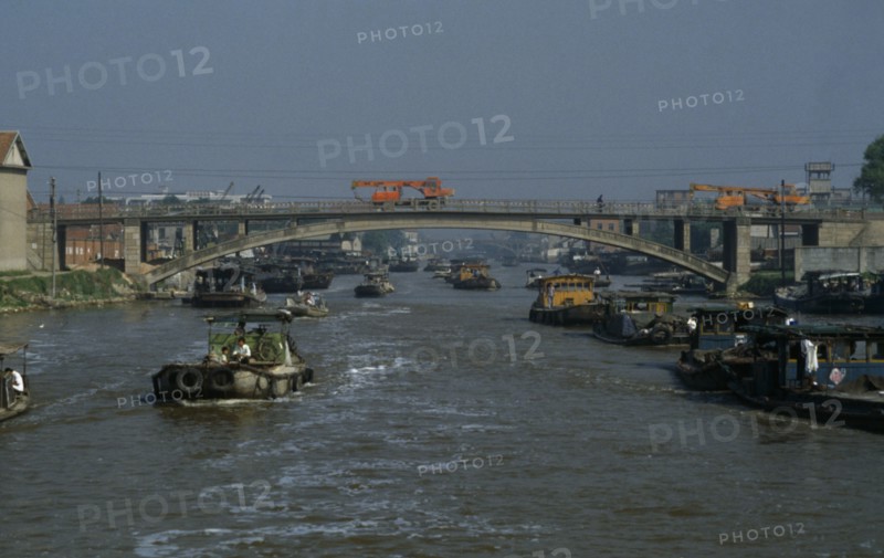 CHINA, Jiangsu Province, Transport, Barges travelling down the Grand Canal between Suzhou and Wuxi. Engineering vehicles driving across bridge over canal.