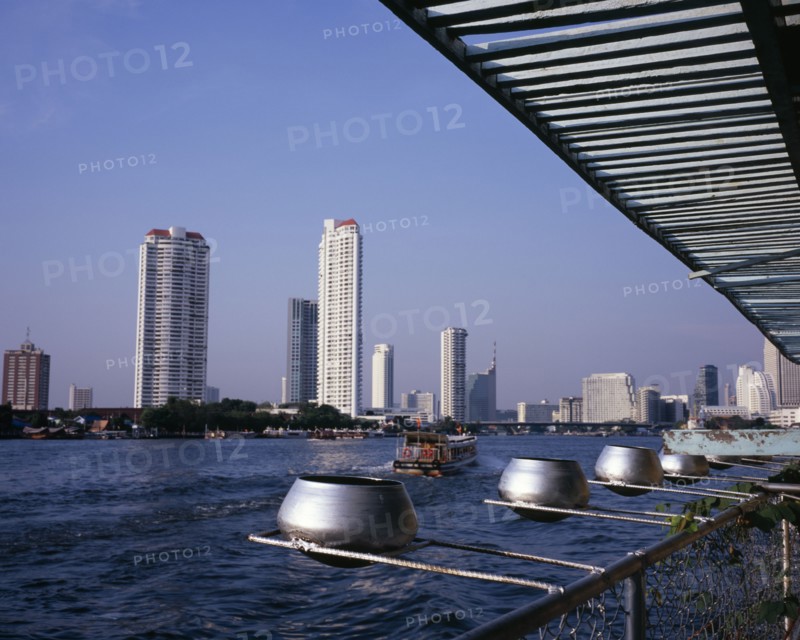 THAILAND, Bangkok, "Chao Phraya River from Wat Ratchasungkhon decorated with silver alms bowls, high rise buildings on opposite bank including Shangri-La hotel and new apartments with river ferry departing north for Saphan Thaksin bridge stop."