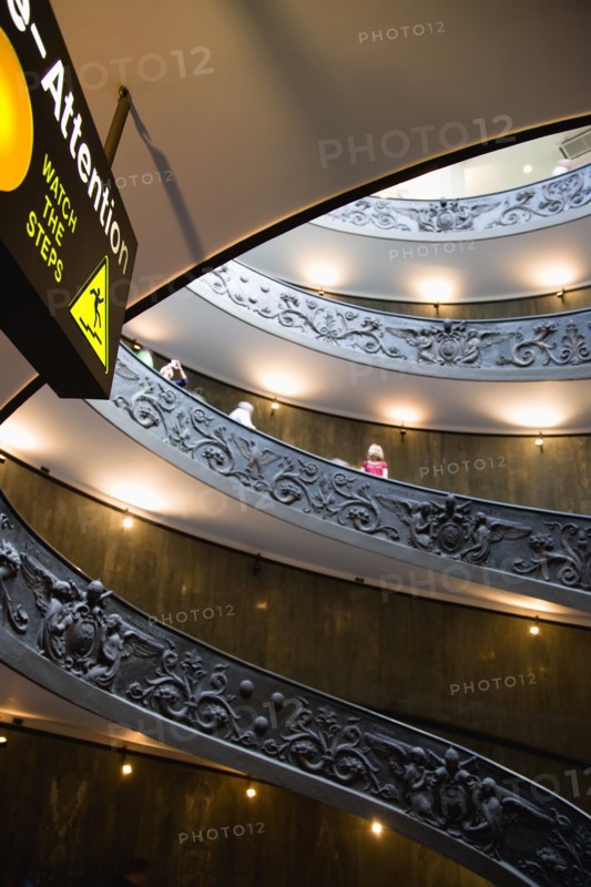 ITALY, Lazio, Rome, Vatican City Museums Tourists descending the Spiral Ramp designed by Giuseppe Momo in 1932 leading from the museums to the street level below seen from below with an illuminated sign warning to watch the steps