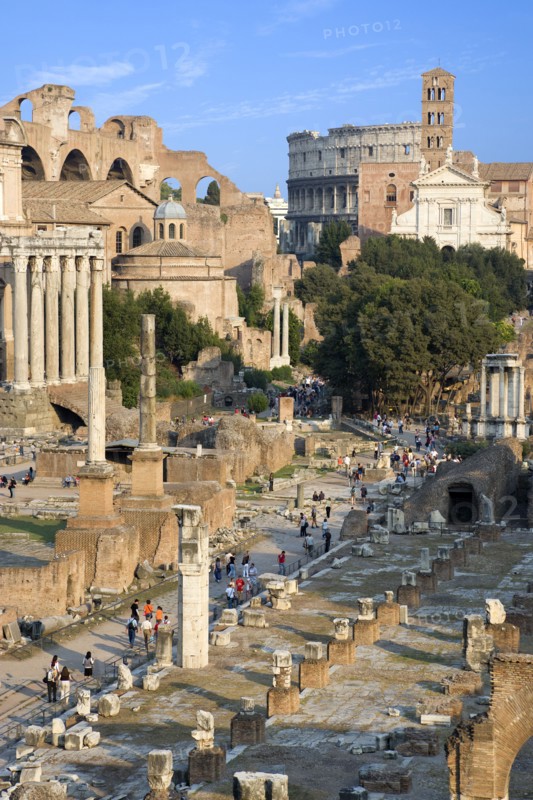 ITALY, Lazio, Rome, View of the Forum with the Colosseum rising behind the bell tower of the church of Santa Francesca Romana with tourists walking past the ruins on the floor of the Forum
