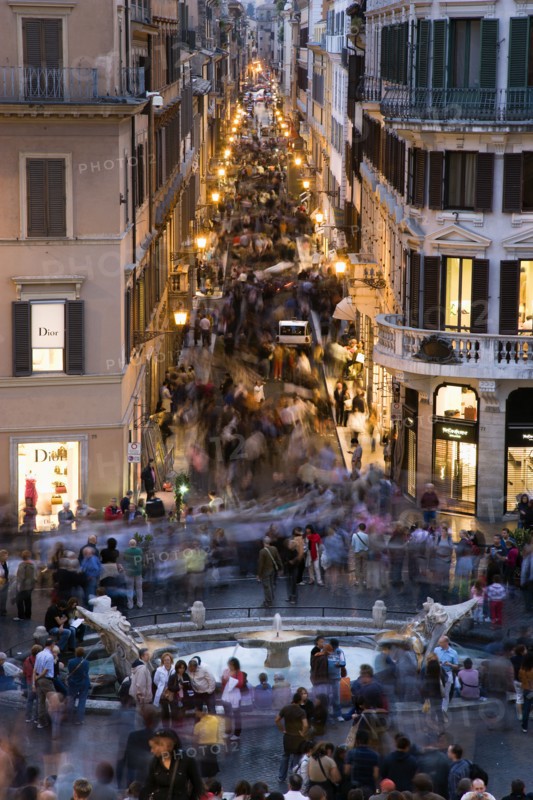 ITALY, Lazio, Rome, The Via dei Condotti the main shopping street busy with people illuminated at night seen from the Spanish Steps with seated tourists and the Fontana della Barcaccia in the foreground