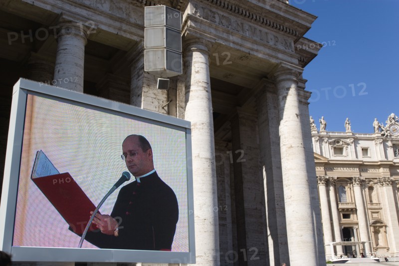 ITALY, Lazio, Rome, Vatican City A cardinal reading from a red book seen on a large video TV monitor display with Pope Benedict XVI Joseph Alois Radzinger seated under a canopy in St Peter's Square for the wednesday Papal Audience in front of the Basilica