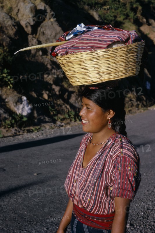 GUATEMALA, Lake Atitlan, Indian girl walking along road carrying a basket of washing on top of her head with a Roman Catholic candle. Near Lake Atitlan