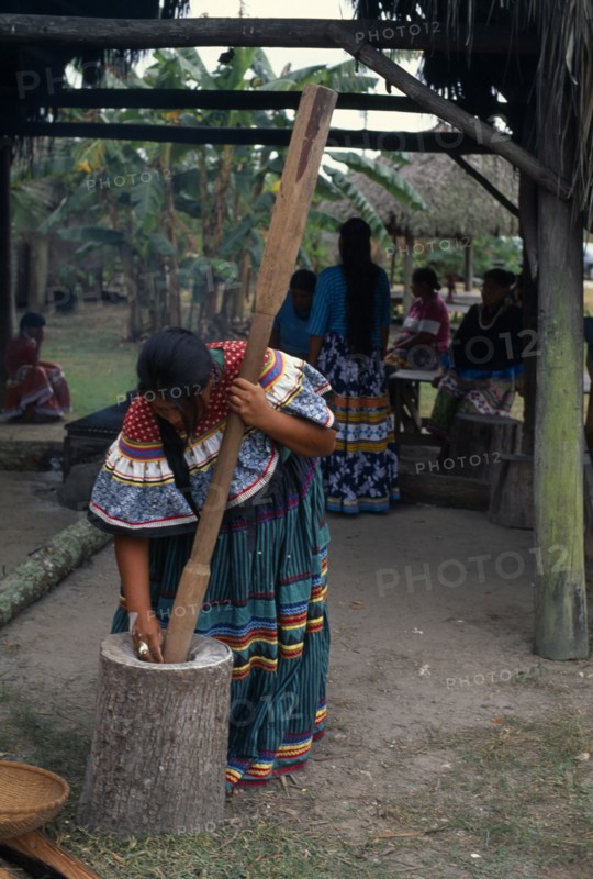 USA, Florida, Everglades, Independent Seminole Native American village. Woman pounding corn wearing traditional colourful patchwork clothing