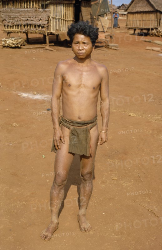 VIETNAM, Central Highlands, Pleimurong village, Vietnam War. Montagnard tribesman in traditional dress in Pleidok refugee camp with typical Montagnard village houses on stilts in background
