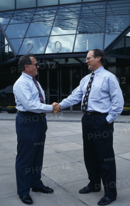 USA, Florida, Orlando, Two businessmen in conversation shaking hands outside modern glass fronted building in downtown business area.